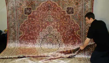 Artisan dépliant un grand tapis persan clair pour repérer les taches à traiter