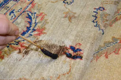 Détachage au pinceau, produit posé au point sur une tache brune d&rsquo;un tapis noué main, à l&rsquo;atelier Tissu Ébène