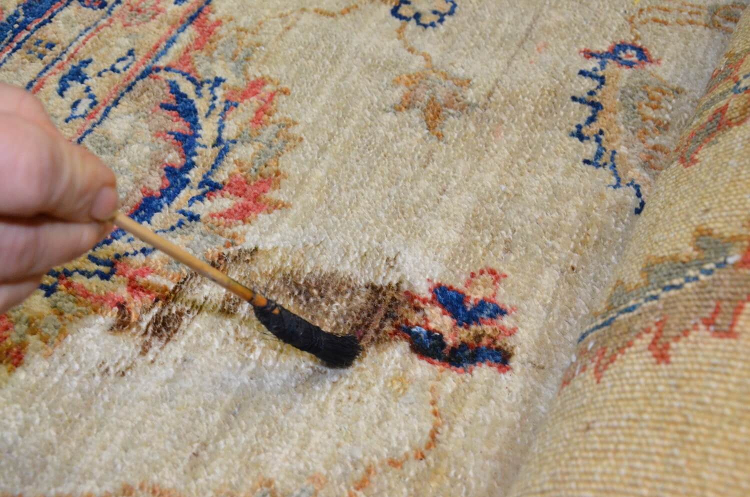Détachage au pinceau, produit posé au point sur une tache brune d&rsquo;un tapis noué main, à l&rsquo;atelier Tissu Ébène