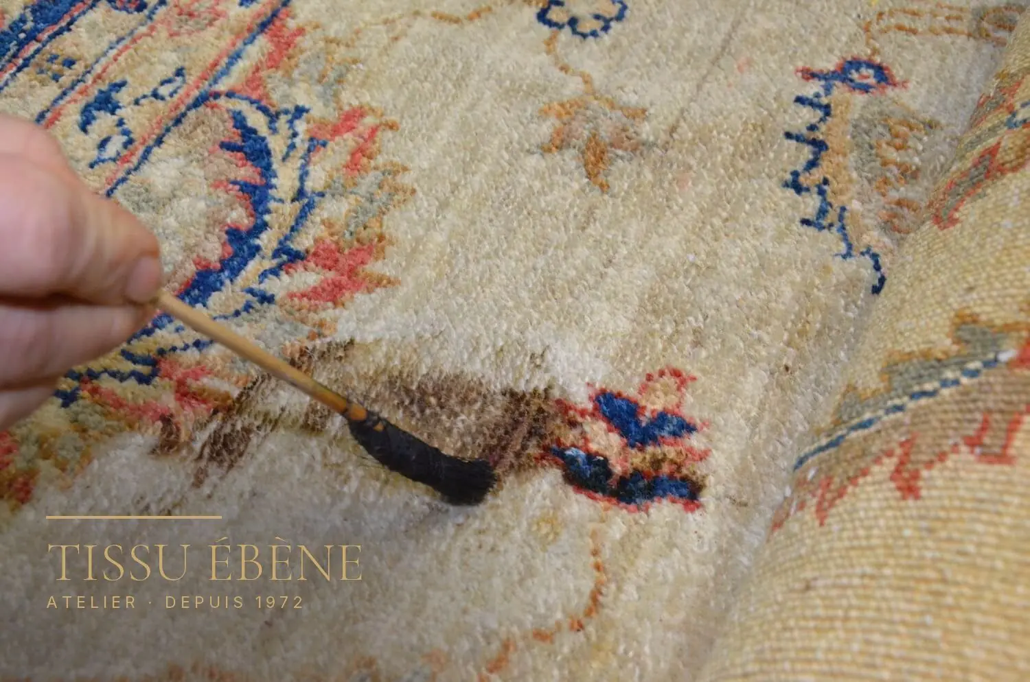 Pinceau brossant une tache sombre sur un tapis à fond ivoire et motifs floraux