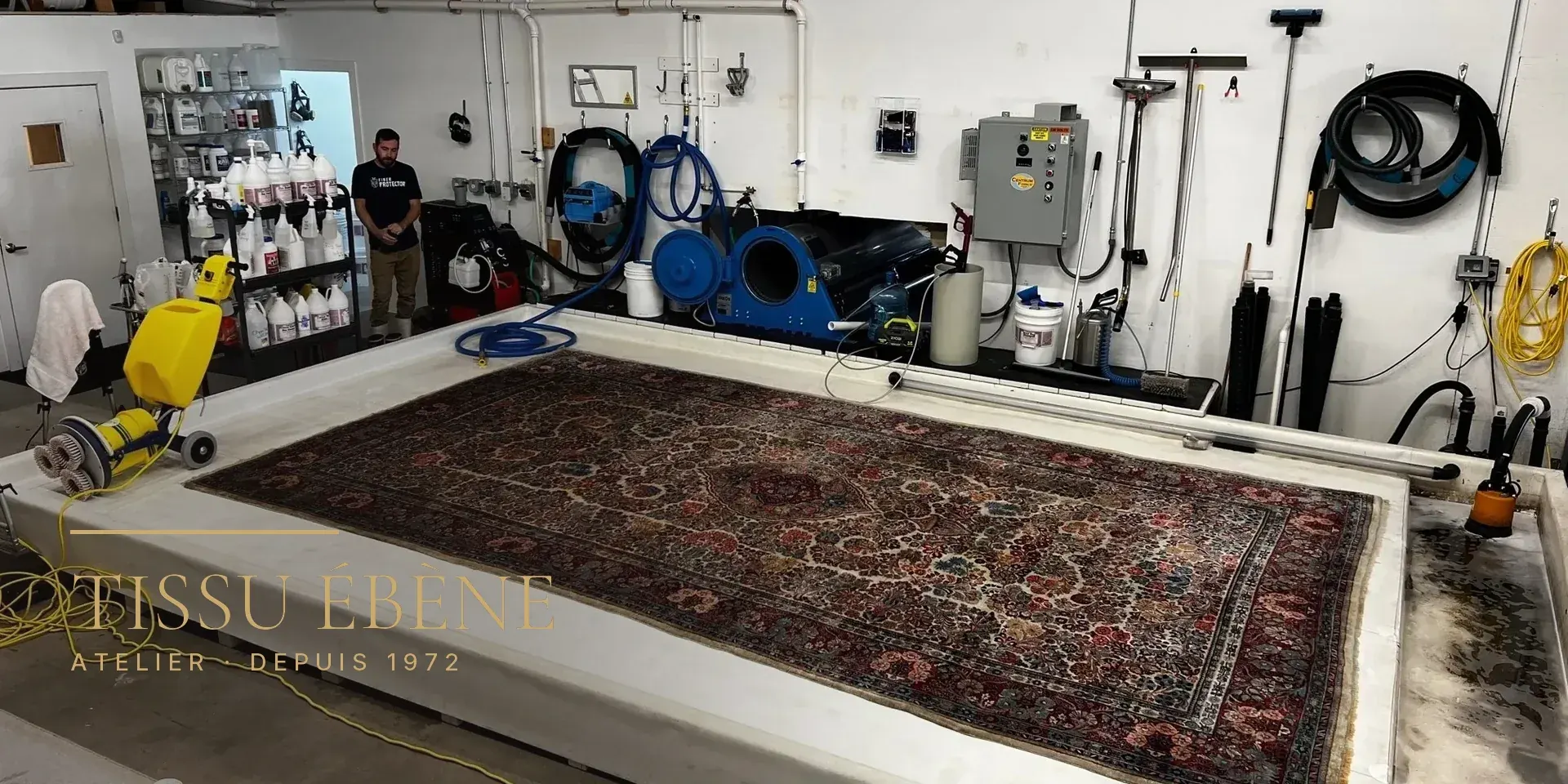 Grand tapis d’Orient à médaillon étendu sur une table de lavage dans un atelier équipé de machines
