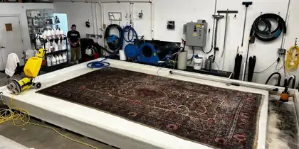 Grand tapis d'Orient posé à plat sur la table de lavage, avant le dépoussiérage