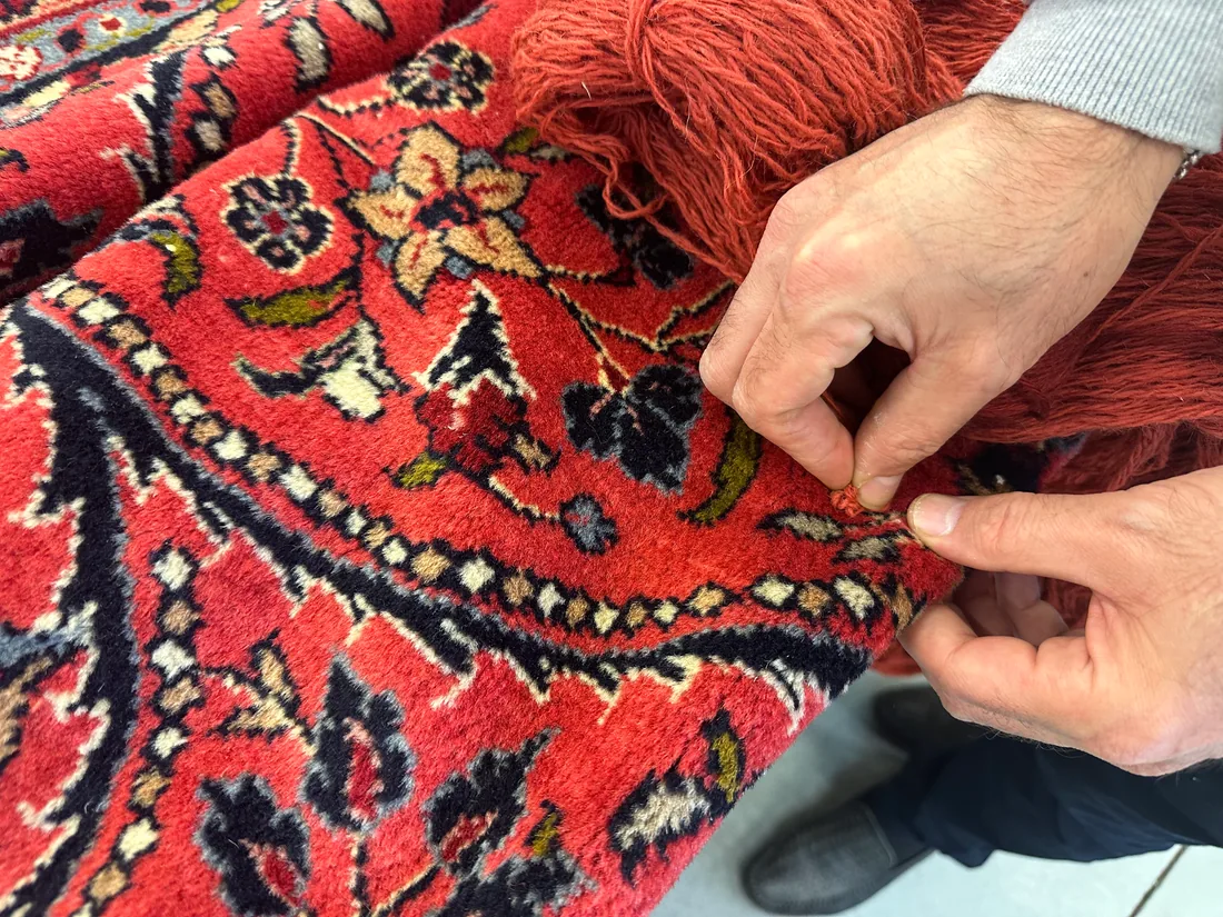 Expert écartant le velours d&rsquo;un tapis persan pour observer le nœud à la base des brins
