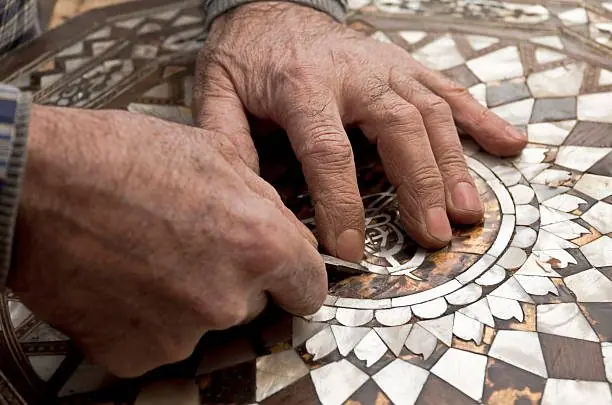 Mains d'artisan incrustant des éclats de nacre dans un plateau marqueté