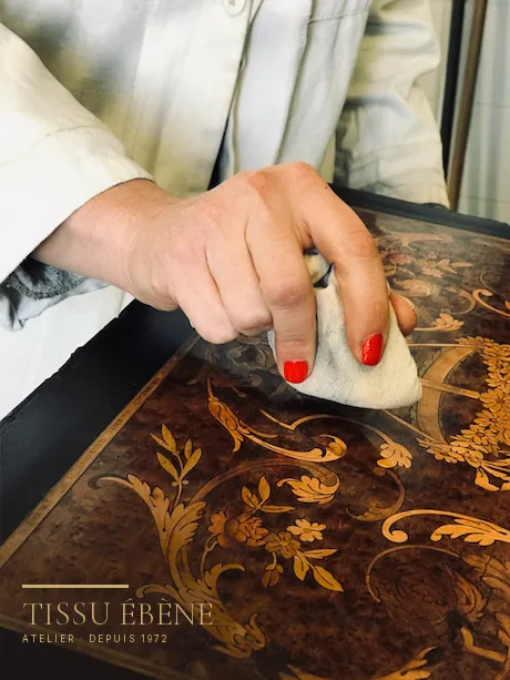 Main polissant au tampon le plateau marqueté d'un meuble ancien