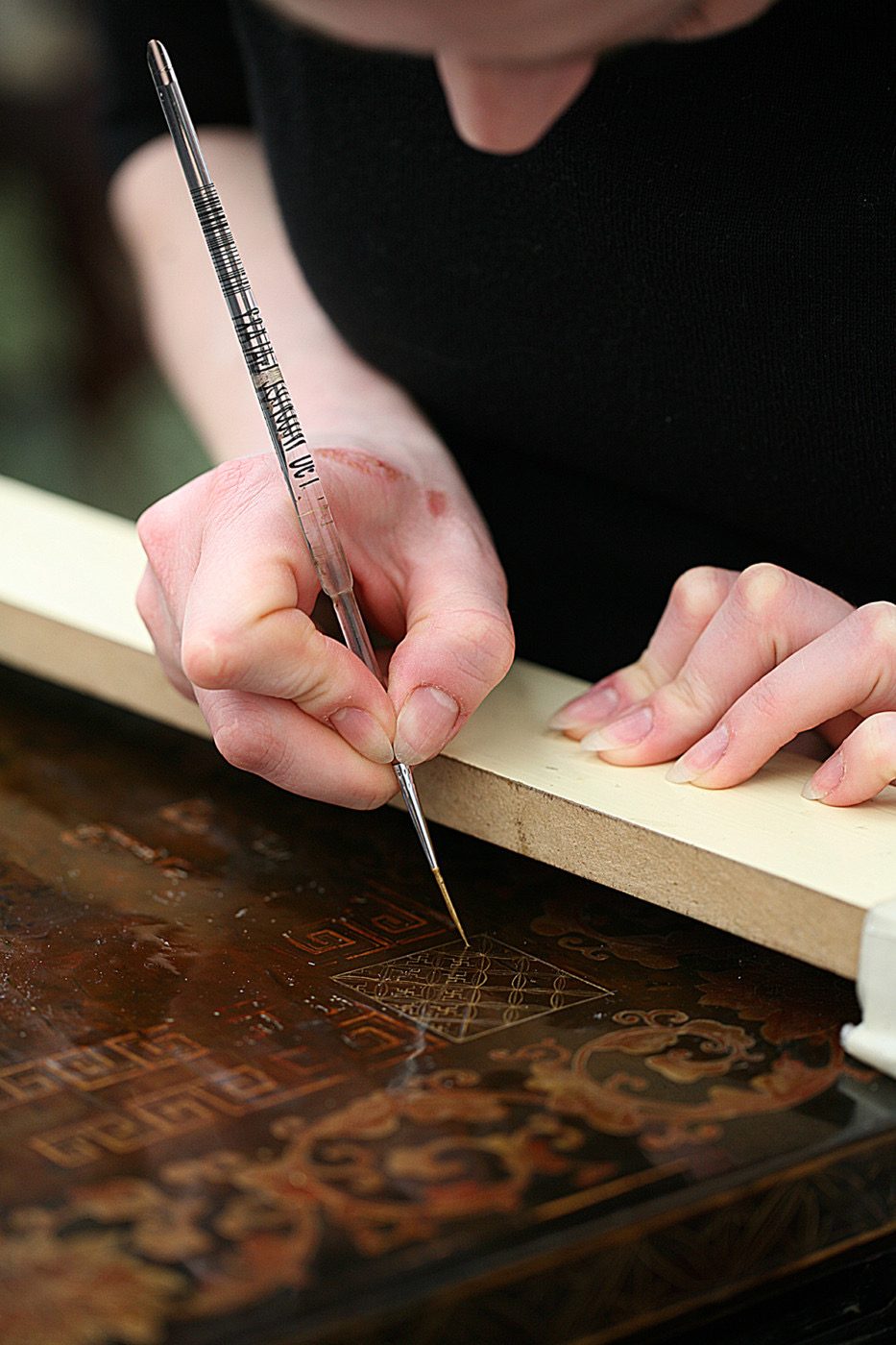 Retouche au pinceau fin d'un décor gravé sur un panneau de laque ancienne