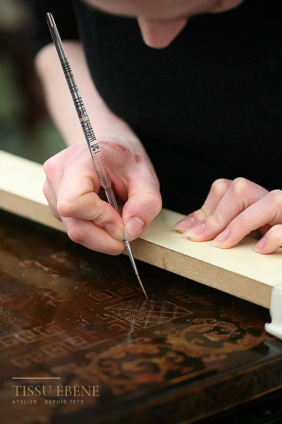 Retouche au pinceau fin d'un décor gravé sur un panneau de laque ancienne