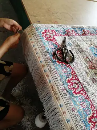 Franges d'un tapis en soie refaites à la main, fil à fil, sur la table de l'atelier