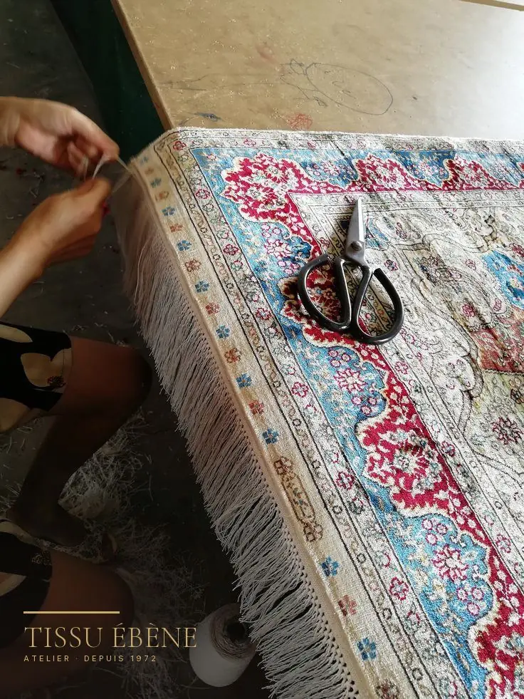 Franges d'un tapis en soie refaites à la main, fil à fil, sur la table de l'atelier