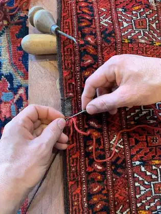 Lisière de tapis reprise à l'aiguille avec une laine teinte au ton de la pièce
