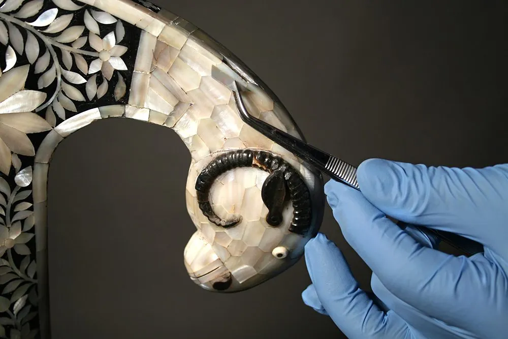 Dépose d'un éclat de nacre à la main sur une tête de bélier sculptée
