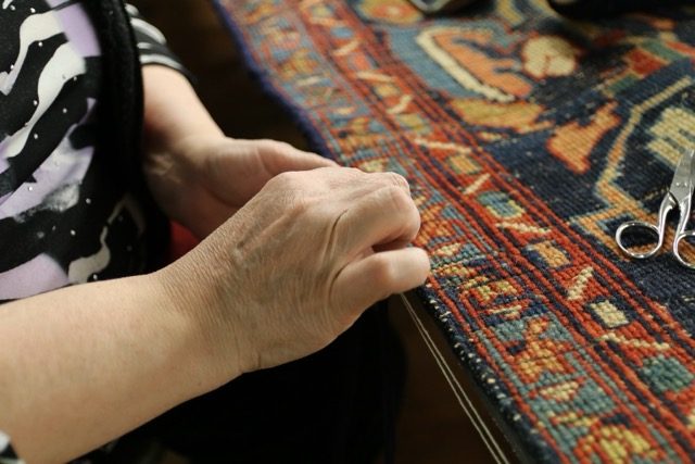 Artisane suivant le bord d’un tapis ancien pour repérer la partie de lisière à reprendre