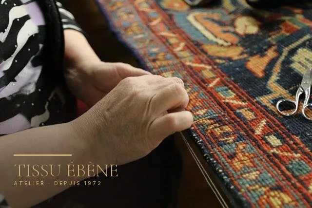 Artisane suivant le bord d’un tapis ancien pour repérer la partie de lisière à reprendre