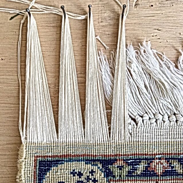 Réparation de franges de tapis : fils de chaîne repris un par un sur base saine, à l&rsquo;atelier
